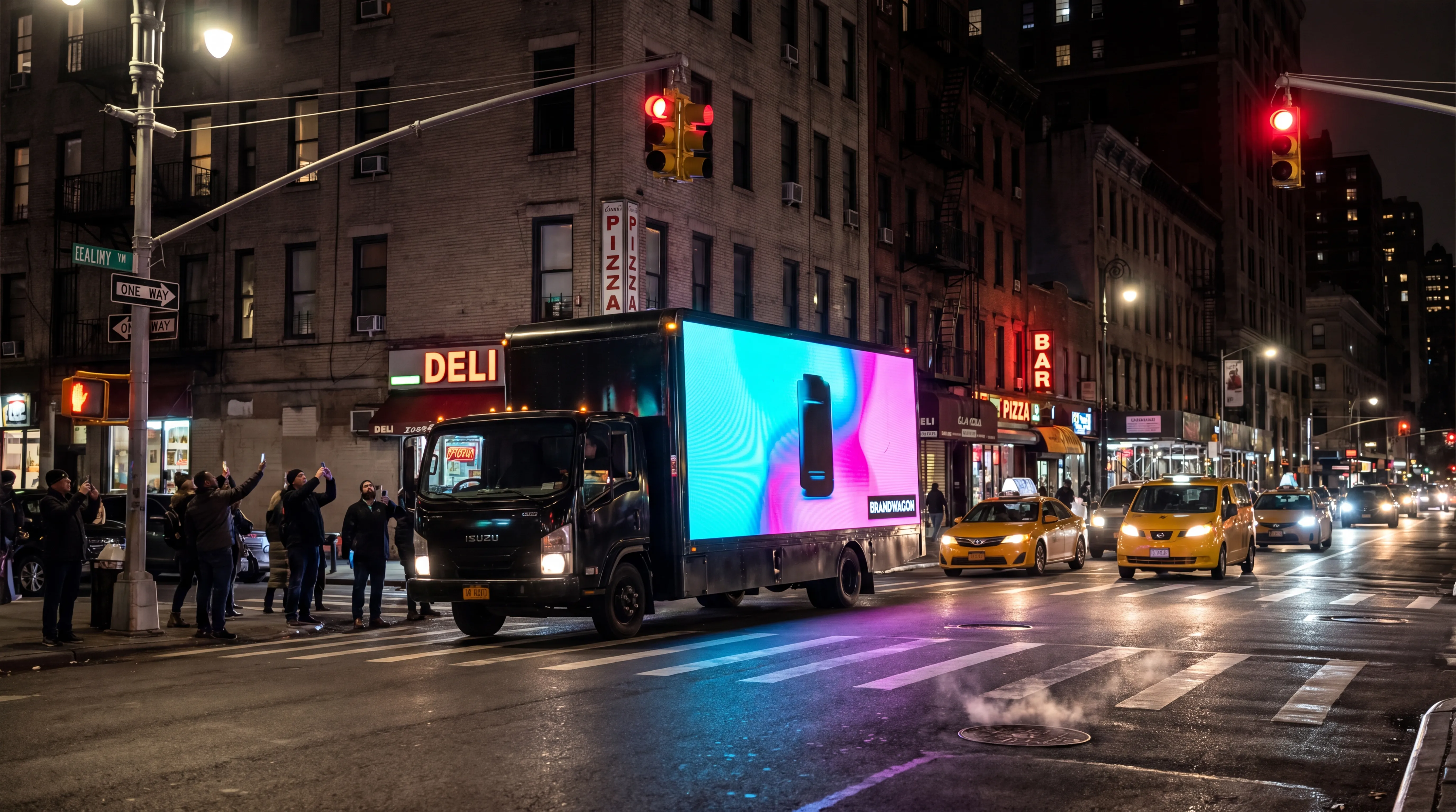 Brandwagon LED billboard truck stopped at a busy urban intersection at night with pedestrians taking phone photos of the bright LED screen
