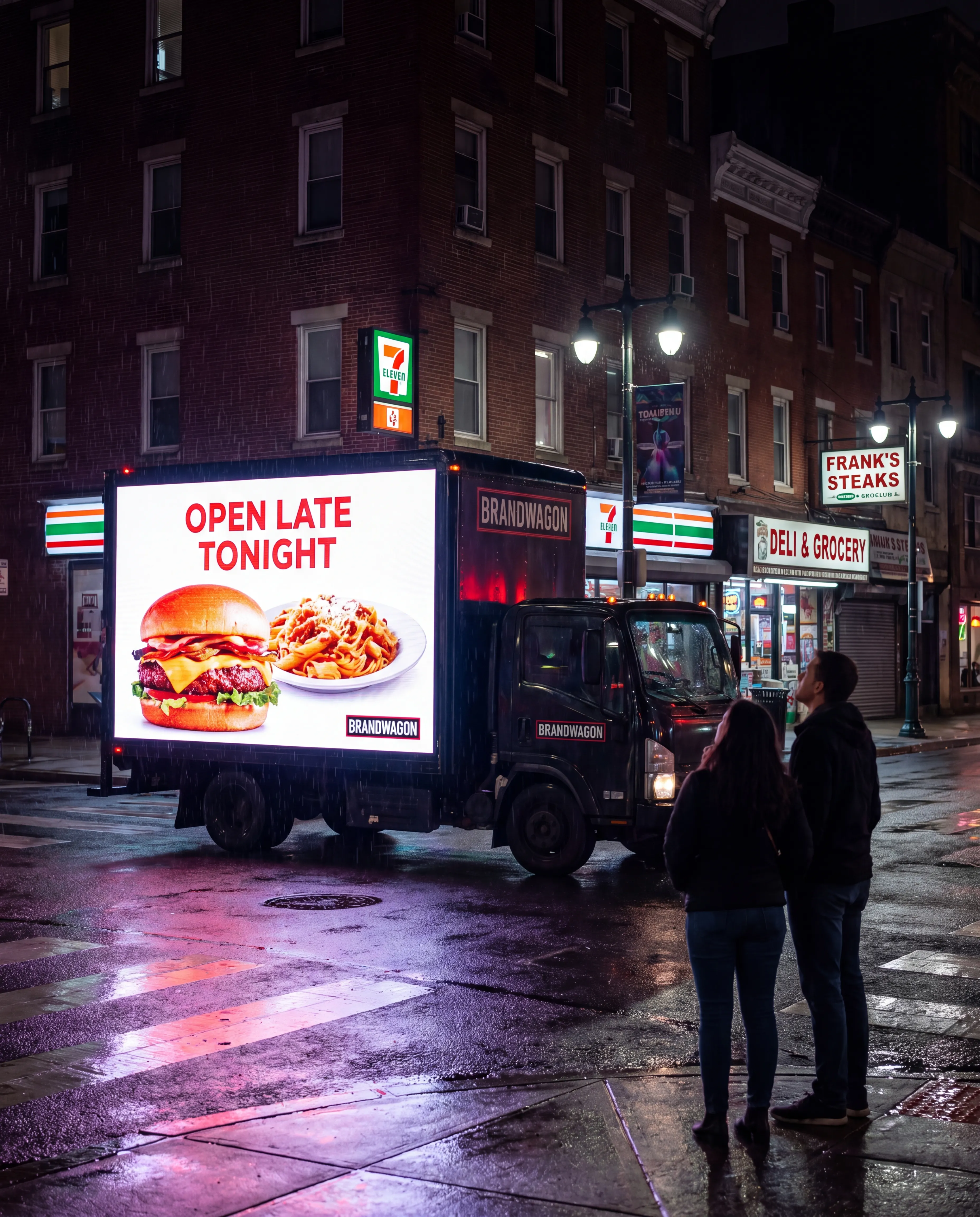 Single Brandwagon LED truck at a Philadelphia street corner at night with OPEN LATE TONIGHT food ad on the screen, a 7-Eleven and deli visible behind